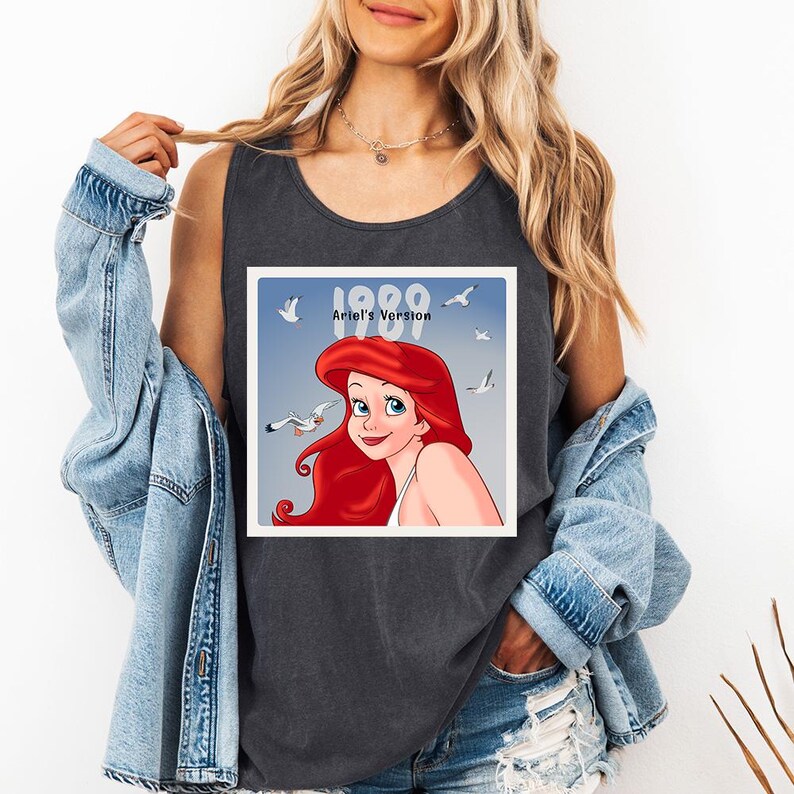 May include: Dark grey tank top featuring a square graphic of Ariel from The Little Mermaid, with red hair and a blue background. The graphic includes the text "1989 Ariel's Version" and images of seagulls.