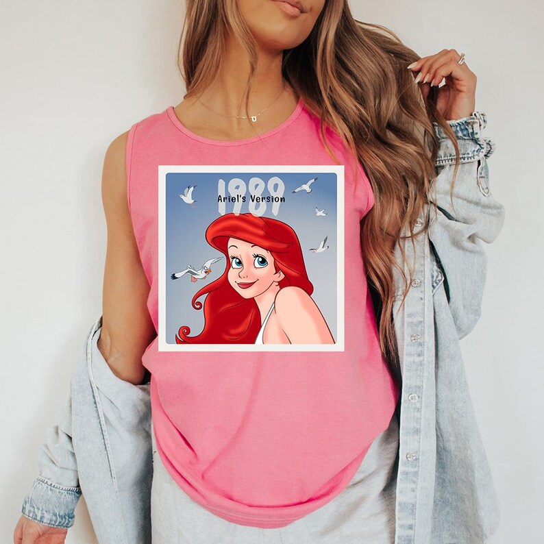 May include: Pink tank top featuring a graphic of Ariel from The Little Mermaid. The graphic includes the text "1989 Ariel's Version" with seagulls in the background. The tank top is sleeveless and made of a soft material.