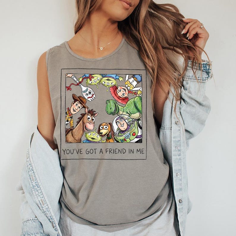 May include: Grey tank top with a framed graphic of Toy Story characters. The image includes Woody, Buzz Lightyear, and other characters from the movie. The text "YOU'VE GOT A FRIEND IN ME" is printed below the graphic.
