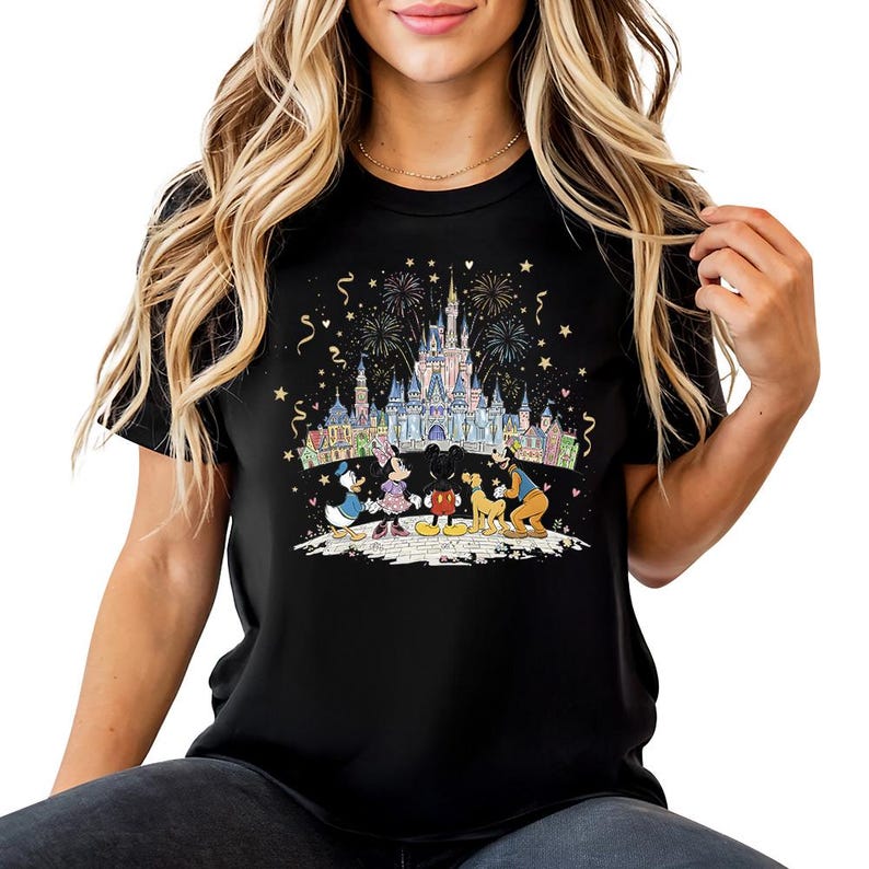 Op de afbeelding: Zwart T-shirt met een kleurrijke afbeelding van een kasteel, vuurwerk en Disney-personages. Het ontwerp bevat Mickey Mouse, Minnie Mouse, Donald Duck en Goofy. Het shirt heeft een ronde hals en korte mouwen.
