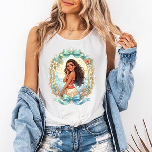 K&ouml;nnte beinhalten: Wei&szlig;es Tanktop mit einer farbenfrohen Illustration einer Frau in einem rot-wei&szlig;en Outfit, umrahmt von einem goldenen Oval mit t&uuml;rkisfarbenen Schleifen und floralen Akzenten. Das Design zeigt eine tropische Szene mit Meereswellen und Palmen.