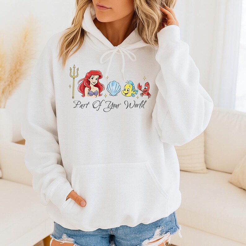 May include: White hooded sweatshirt featuring a colorful graphic of a trident, a mermaid, a seashell, a yellow fish, and a red crab. The text "Part of Your World" is below the graphic. The sweatshirt has a front pocket and a drawstring hood.