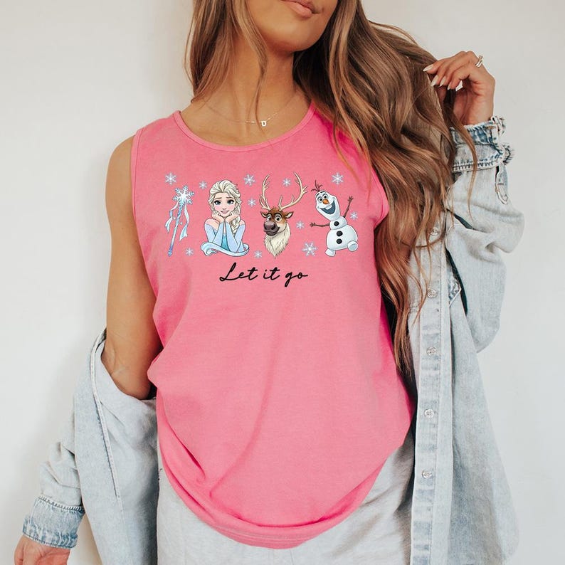 May include: Pink tank top featuring cartoon characters from the movie Frozen, including Elsa, Olaf, and Sven, with snowflakes and the phrase "Let it go" in black script. The shirt is sleeveless.