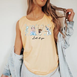 May include: A light yellow tank top featuring a graphic of characters from the movie Frozen, including Elsa, Olaf, and Sven. The phrase "Let it go" is written in black script below the characters. The tank top is sleeveless.