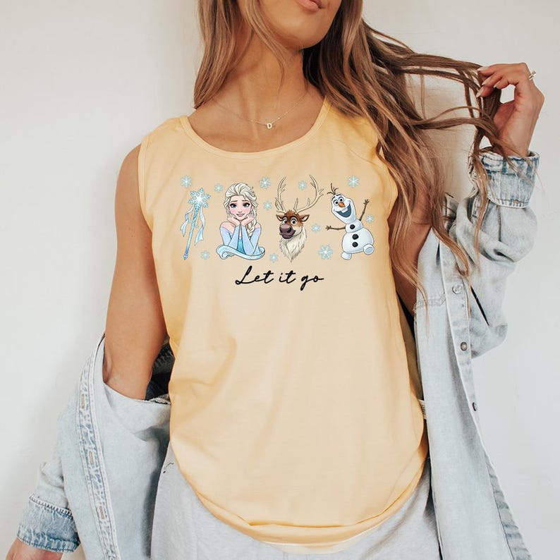 May include: A light yellow tank top featuring a graphic of characters from the movie Frozen, including Elsa, Olaf, and Sven. The phrase "Let it go" is written in black script below the characters. The tank top is sleeveless.