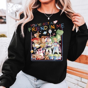 May include: Black sweatshirt featuring a colorful graphic of characters from the animated film "Toy Story." The text "YOU'VE GOT A FRIEND IN ME" is displayed above the characters. The design includes Woody, Buzz Lightyear, and other beloved characters.