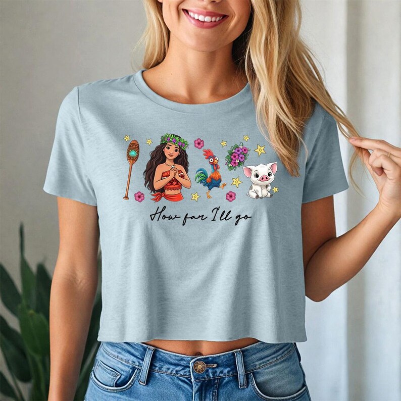 May include: Pale blue crop top with a vibrant graphic. The design includes characters and the text "How far I'll go". The graphic features a character with a flower crown, a rooster, a pig, and other elements.