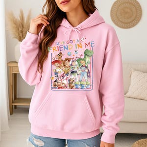 May include: Pink hooded sweatshirt featuring a graphic of characters from the animated film "Toy Story." The graphic includes Woody, Buzz Lightyear, and other characters, with the text "YOU'VE GOT A FRIEND IN ME."