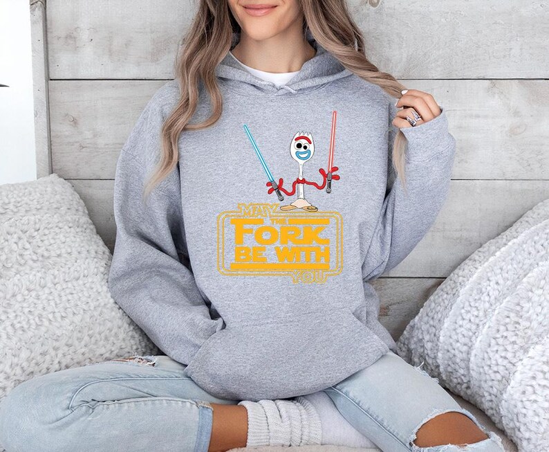 May include: A heather gray hooded sweatshirt featuring a graphic of a white plastic spork character with red pipe cleaner arms. The character holds a blue and a red lightsaber. Below, yellow text reads: MAY THE FORK BE WITH YOU.