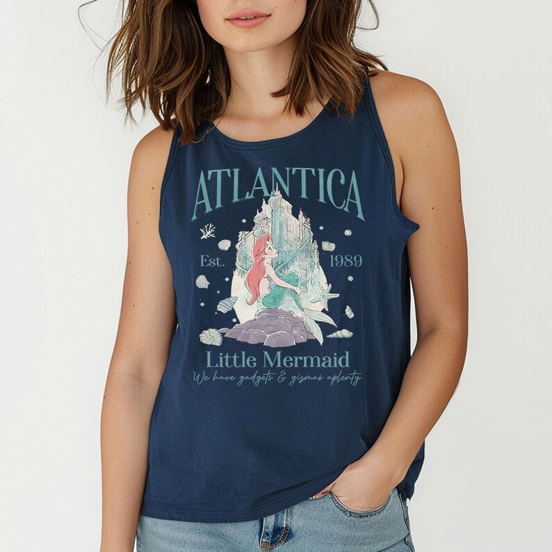 Op de afbeelding: Marineblauwe tanktop met een afbeelding van de Kleine Zeemeermin. Het ontwerp bevat het woord "Atlantica" boven een illustratie van de zeemeermin en een kasteel. De tekst "Est. 1989" en "We have gadgets & gizmos aplenty" zijn ook opgenomen.