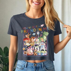 May include: A navy blue crop top with a colourful graphic of Toy Story characters. The text "YOU'VE GOT A FRIEND IN ME" is above the characters. The top is worn with blue jeans.