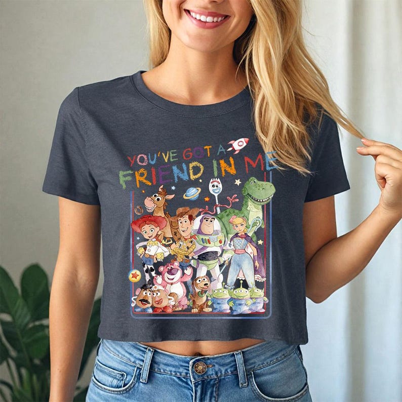 May include: A navy blue crop top with a colourful graphic of Toy Story characters. The text "YOU'VE GOT A FRIEND IN ME" is above the characters. The top is worn with blue jeans.
