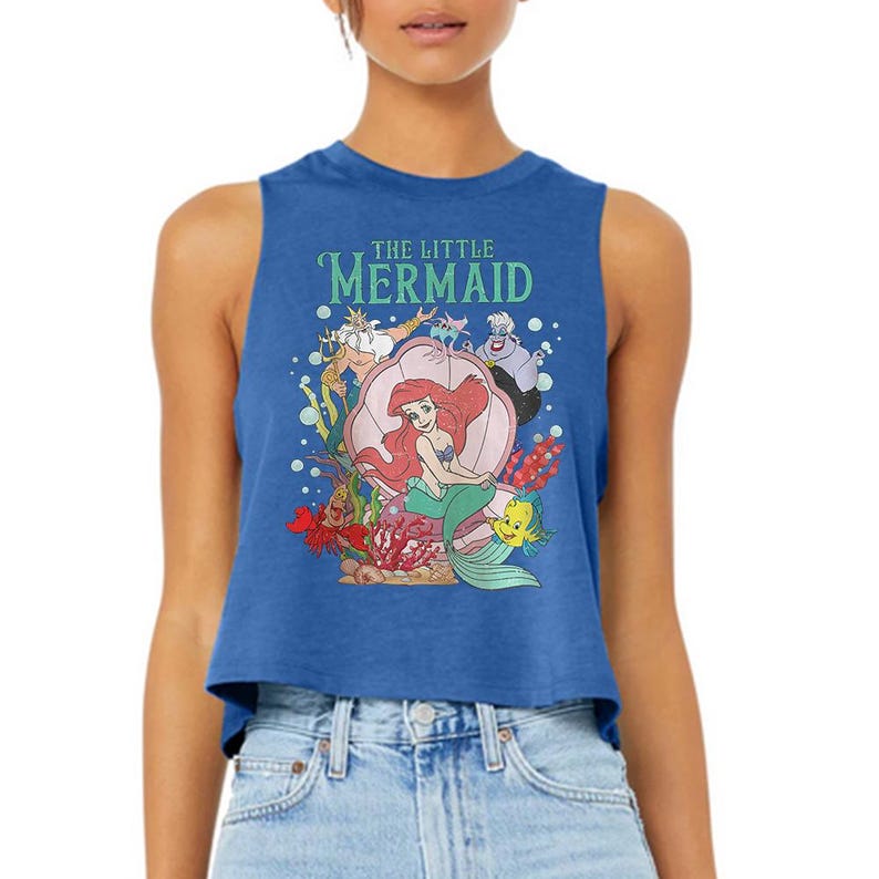 Puede incluir: Un top corto sin mangas de color azul real con un estampado gr&aacute;fico de los personajes de La Sirenita, incluyendo a Ariel, el Rey Trit&oacute;n, &Uacute;rsula, Sebasti&aacute;n y Flounder. El dise&ntilde;o incluye el texto THE LITTLE MERMAID en letras verde claro.