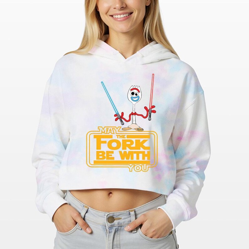 May include: A white and pastel tie-dye cropped hoodie featuring a graphic of a spork character holding a blue and a red lightsaber. Below the character, the yellow text reads MAY THE FORK BE WITH YOU, styled in a classic science fiction movie font.