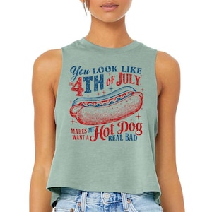 Peut inclure: Un haut court sans manches vert clair avec le texte "You look like the 4th of July" et "Makes me want a Hot Dog real bad." Un dessin d'un hot-dog est au centre du motif.