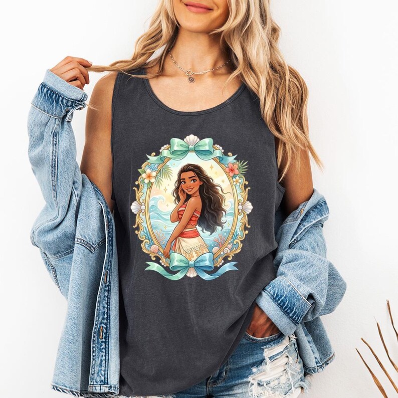 K&ouml;nnte beinhalten: Dunkelgraues Tanktop mit einer farbenfrohen Illustration einer Frau in tropischer Umgebung, umrahmt von einem goldenen Oval mit Blumen und Schleifen. Die Frau hat lange dunkle Haare und tr&auml;gt ein rot-wei&szlig;es Outfit.