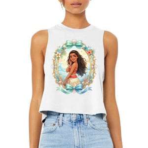 Puede incluir: Top corto sin mangas blanco con una colorida ilustraci&oacute;n de una mujer con un atuendo rojo y blanco, enmarcada por un &oacute;valo dorado con flores y lazos verde azulado. El dise&ntilde;o incluye olas del oc&eacute;ano.