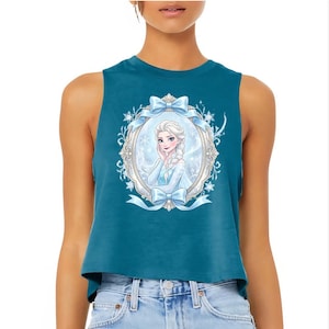 Pu&ograve; includere: Top corto color teal con un'illustrazione incorniciata di una principessa con capelli biondi e un vestito blu. La cornice &egrave; decorata con fiocchi e fiocchi di neve. Il top &egrave; senza maniche e realizzato in materiale morbido.