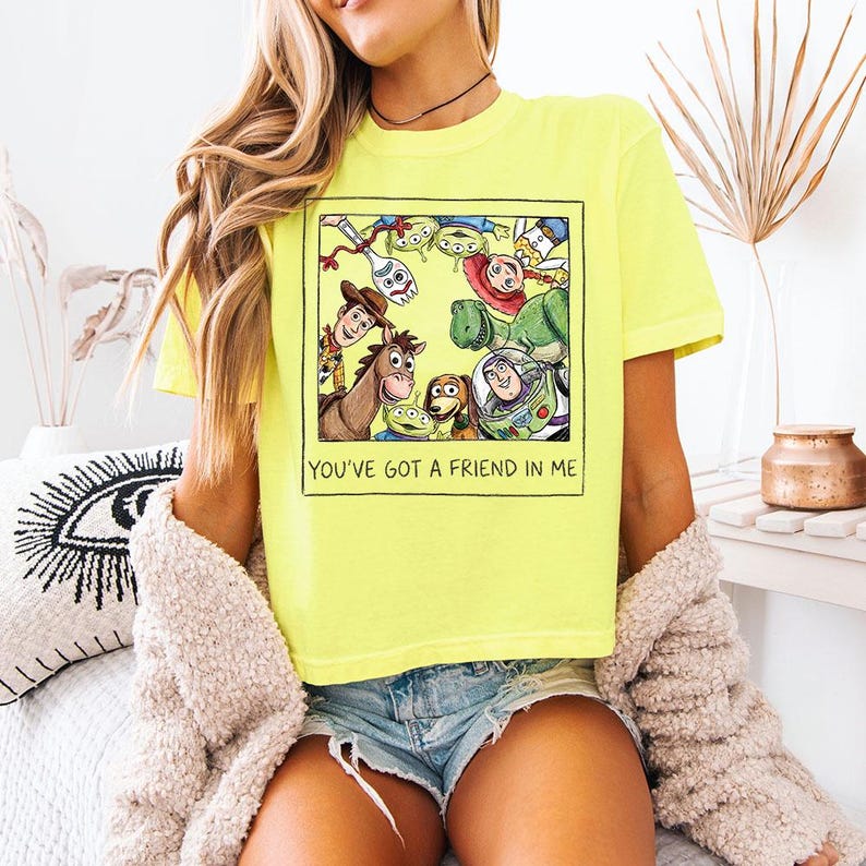 May include: A bright yellow t-shirt with a graphic of Toy Story characters in a black frame. The text "YOU'VE GOT A FRIEND IN ME" is below the image. The shirt is a vibrant colour.