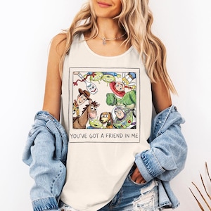 May include: Cream-coloured vest top with a framed illustration of characters from the animated film "Toy Story." The image includes Woody, Buzz Lightyear, and other characters. The text "YOU'VE GOT A FRIEND IN ME" is printed below the illustration.