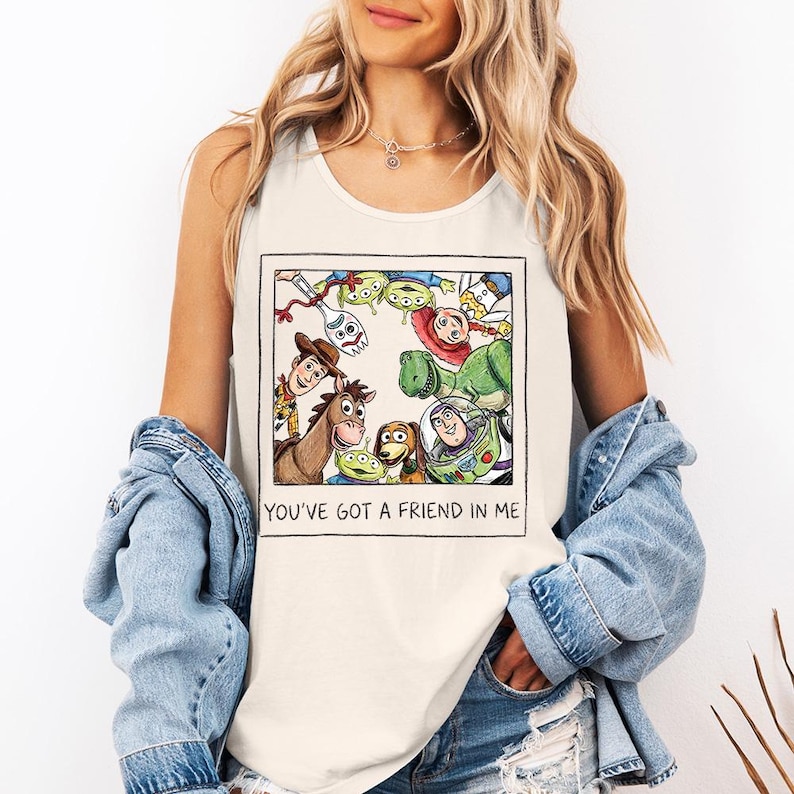 May include: Cream-coloured vest top with a framed illustration of characters from the animated film "Toy Story." The image includes Woody, Buzz Lightyear, and other characters. The text "YOU'VE GOT A FRIEND IN ME" is printed below the illustration.
