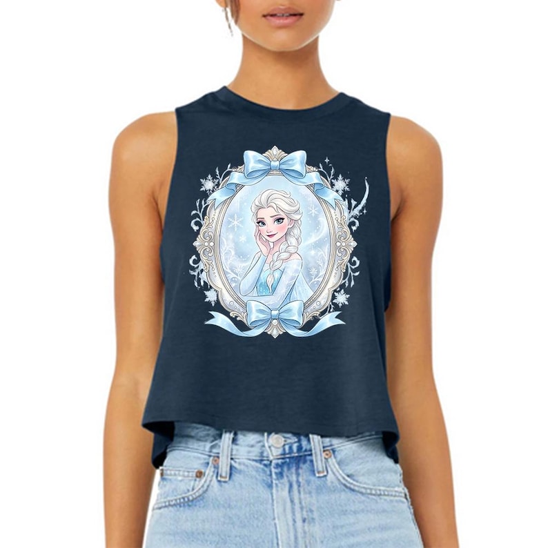 Pu&ograve; includere: Top corto blu navy con un'illustrazione incorniciata di un personaggio dei cartoni animati con capelli biondi e un vestito blu. La cornice &egrave; decorata con fiocchi blu e dettagli floreali. Il top &egrave; senza maniche e ha uno scollo tondo.