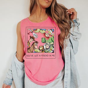 May include: Pink vest top with a framed graphic of Toy Story characters, including Woody, Buzz Lightyear, and the aliens. The text "YOU'VE GOT A FRIEND IN ME" is printed below the graphic. The top is sleeveless.