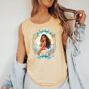 K&ouml;nnte beinhalten: Ein hellgelbes Tanktop mit einer Cartoon-Illustration einer Frau in einem rot-wei&szlig;en Outfit, umrahmt von einem goldenen Oval mit floralen und Wellen-Akzenten. Das Design beinhaltet t&uuml;rkisfarbene Schleifen.