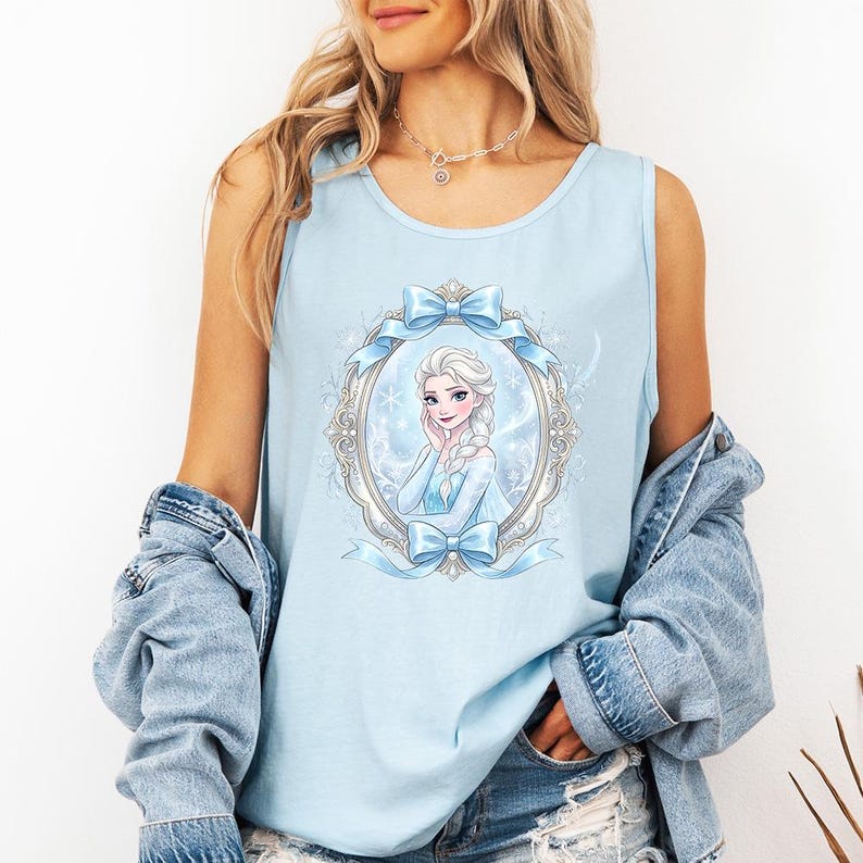 May include: Light blue tank top featuring a framed illustration of a princess with blonde hair and a blue dress. The frame is adorned with blue bows and ribbons. The tank top is sleeveless and made of a soft material.