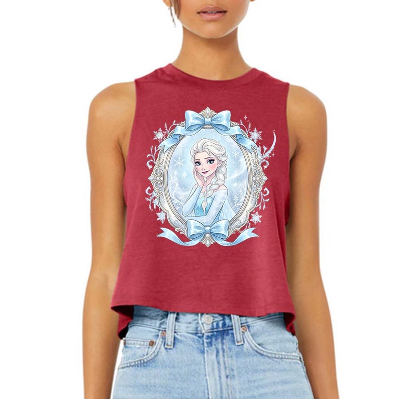 Pu&ograve; includere: Un top corto senza maniche bordeaux con un'illustrazione incorniciata di una donna dei cartoni animati con trecce bionde, che indossa un vestito blu. La cornice &egrave; decorata con fiocchi blu e fiocchi di neve. Il top &egrave; realizzato in materiale morbido.