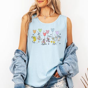 May include: Pale blue vest top with a colourful graphic of Disney characters holding Mickey Mouse-shaped balloons. Characters include Pluto, Mickey Mouse, Minnie Mouse, Donald Duck, and Daisy Duck. The text "Mickey Mouse" is also present.