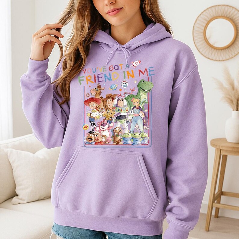 May include: A light purple hoodie featuring a colorful graphic of characters from the movie Toy Story. The graphic includes the text "YOU'VE GOT A FRIEND IN ME". The hoodie has a front pocket and a drawstring hood.