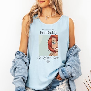 May include: Light blue tank top with the text "But Daddy" and "I Love Him". The tank top features a graphic of a cartoon character with red hair. The tank top is made of a soft material.
