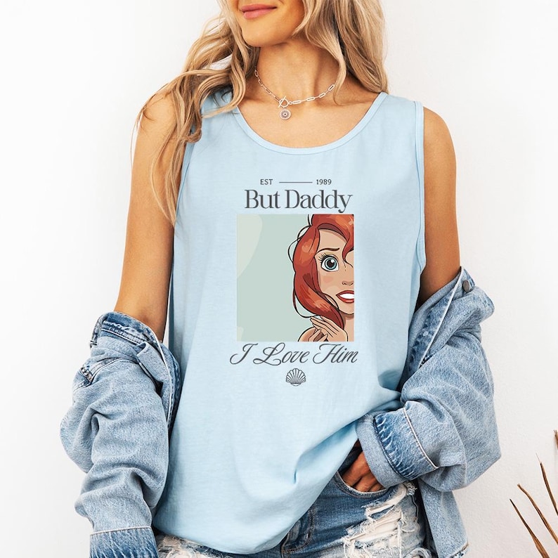 May include: Light blue tank top with the text "But Daddy" and "I Love Him". The tank top features a graphic of a cartoon character with red hair. The tank top is made of a soft material.