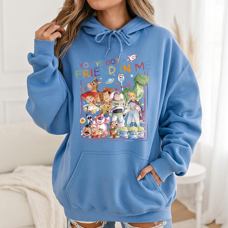 May include: A light blue hoodie featuring a colorful graphic of characters from a popular animated movie. The graphic includes the text "YOU'VE GOT A FRIEND IN ME". The hoodie has a drawstring hood and a front pocket.