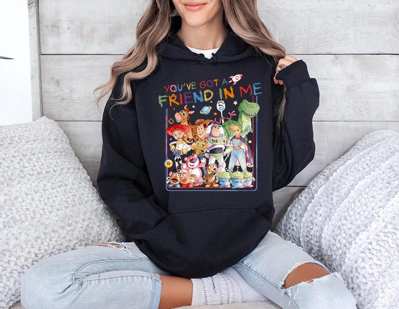 May include: A navy blue hooded sweatshirt featuring a colorful graphic of characters from a popular animated movie. The text "YOU'VE GOT A FRIEND IN ME" is printed above the graphic. The sweatshirt is worn by a person.