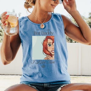 May include: Light blue tank top with the text "But Daddy" and "I Love Him". The graphic features a cartoon image of a character with red hair and blue eyes. The tank top is made of a soft material.