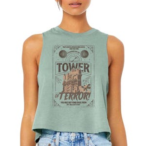 May include: A light green sleeveless crop top featuring a vintage-style graphic for the Tower of Terror ride. The graphic includes the words "Tower of Terror" and other text, along with an illustration of the building.