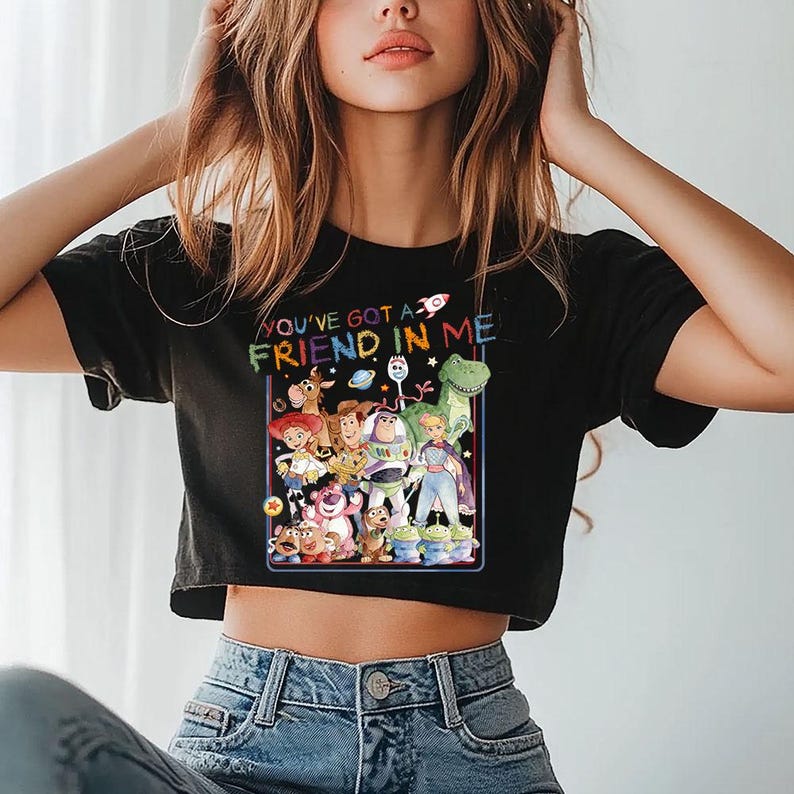May include: Black crop top with a vibrant graphic of characters from the film "Toy Story." The design includes Woody, Buzz Lightyear, and other characters, with the text "YOU'VE GOT A FRIEND IN ME" in rainbow colours.