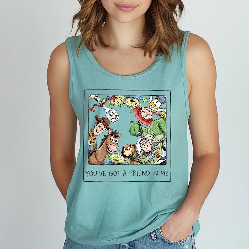 May include: A teal vest top with a framed graphic of characters from the animated film Toy Story. The graphic includes Woody, Buzz Lightyear, and other characters. The text "YOU'VE GOT A FRIEND IN ME" is below the graphic.