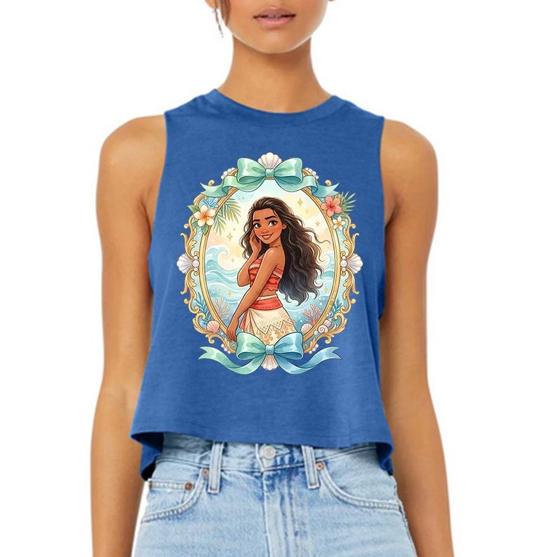 Puede incluir: Top corto azul con una ilustraci&oacute;n enmarcada de una mujer de dibujos animados con cabello largo y oscuro, vestida con un atuendo rojo y blanco, ambientada en una escena de playa tropical. El marco est&aacute; adornado con lazos, flores y conchas marinas.
