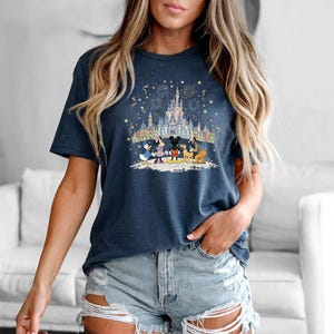 Op de afbeelding: Marineblauw T-shirt met een kleurrijke afbeelding van een kasteel, vuurwerk en Disney-personages. Het ontwerp bevat Mickey Mouse, Minnie Mouse, Donald Duck, Goofy en Pluto. Het shirt is een comfortabele, casual stijl.