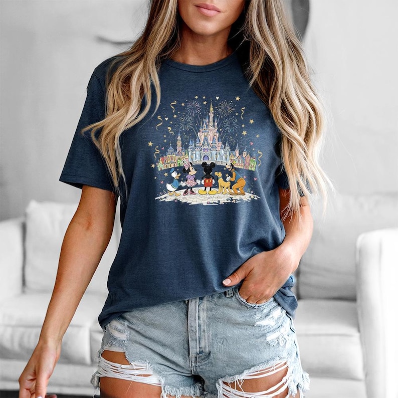 Op de afbeelding: Marineblauw T-shirt met een kleurrijke afbeelding van een kasteel, vuurwerk en Disney-personages. Het ontwerp bevat Mickey Mouse, Minnie Mouse, Donald Duck, Goofy en Pluto. Het shirt is een comfortabele, casual stijl.