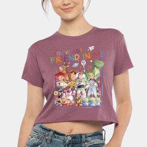 May include: Mauve crop top with a colourful graphic of "Toy Story" characters. The graphic includes the text "YOU'VE GOT A FRIEND IN ME" with a rocket ship and other space-themed elements.