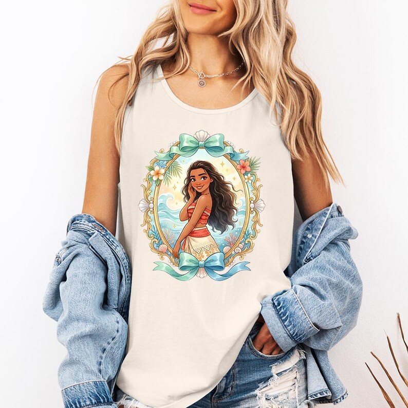 K&ouml;nnte beinhalten: Cremefarbenes Tanktop mit einer Cartoon-Illustration einer Frau in einem rot-wei&szlig; gestreiften Oberteil und einem wei&szlig;en Rock, umrahmt von einem goldenen Oval mit t&uuml;rkisfarbenen Schleifen, Blumen und Muscheln. Die Frau hat lange, dunkle Haare und l&auml;chelt. Der Hintergrund zeigt eine Strandszene.