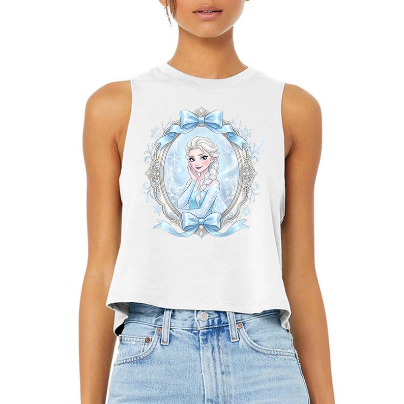 Pu&ograve; includere: Top corto senza maniche bianco con un'illustrazione a cartoni animati di una principessa in una cornice ovale decorativa con fiocchi blu e fiocchi di neve. La principessa ha i capelli bianchi e indossa un vestito blu.