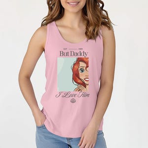 May include: Pink tank top with the text "But Daddy" and "I Love Him". The graphic features a cartoon image of a red-haired woman. The tank top is sleeveless and has a scoop neck.