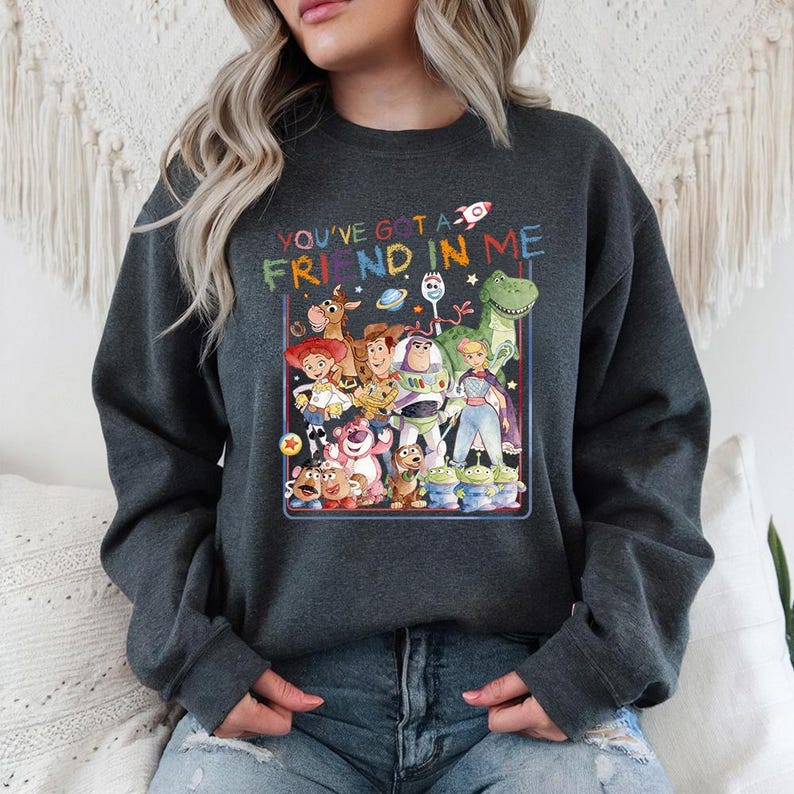 May include: Dark gray sweatshirt featuring a colorful graphic of characters from the animated film "Toy Story." The graphic includes the text "You've Got a Friend in Me" in rainbow colors, along with a rocket ship and other playful elements.