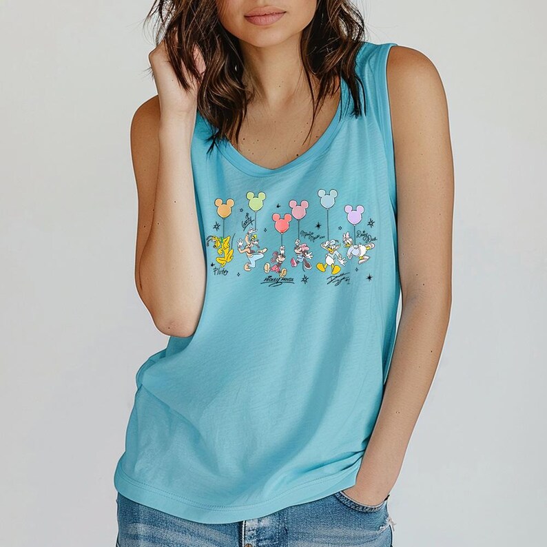 May include: A turquoise tank top with a Disney-themed graphic. The design shows various characters, including Mickey and Minnie Mouse, holding Mickey Mouse-shaped balloons. The top has a scoop neck and a loose fit. The graphic is in multiple colours.