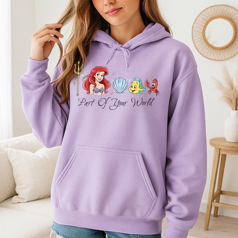 May include: A lilac-colored hoodie featuring a graphic of Ariel, a seashell, Flounder, and Sebastian from The Little Mermaid. The phrase "Part of Your World" is printed below the characters. The hoodie has a front pocket and a drawstring hood.